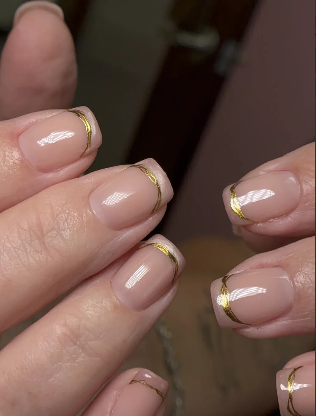 Glossy nude square nails with thin metallic gold curved lines at the tips by Polished by Kim