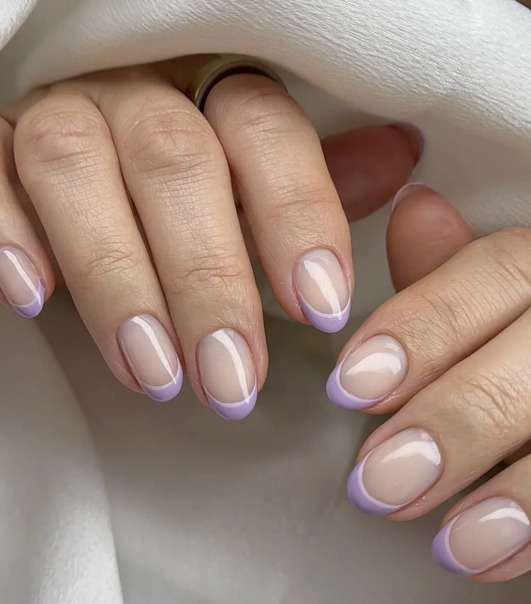 Short round nails with a sheer pink base and delicate thin lavender French tips by Polished by Kim