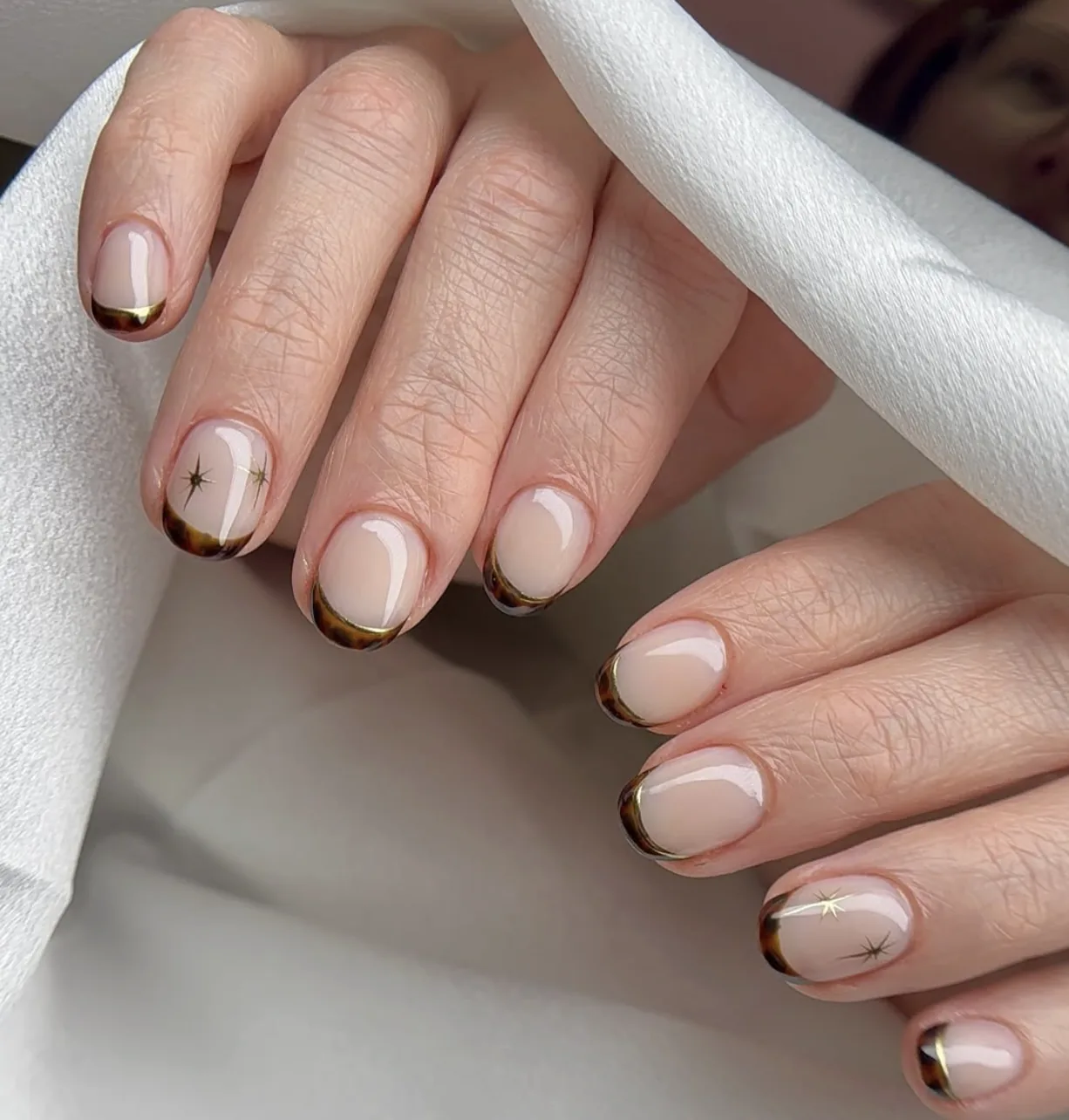Round nude nails with tortoiseshell French tips and delicate gold starburst accents by Polished by Kim